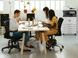 Three colleagues working at co-working desk with printer in background